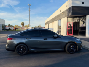 A technician applying clear paint protection film to the front bumper of a high-end vehicle.