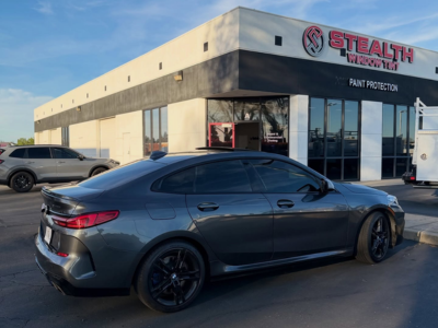 A technician applying clear paint protection film to the front bumper of a high-end vehicle.