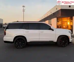 A side profile view of the white luxury SUV, showcasing the uniform dark window tint against the white body and black accents at sunset.